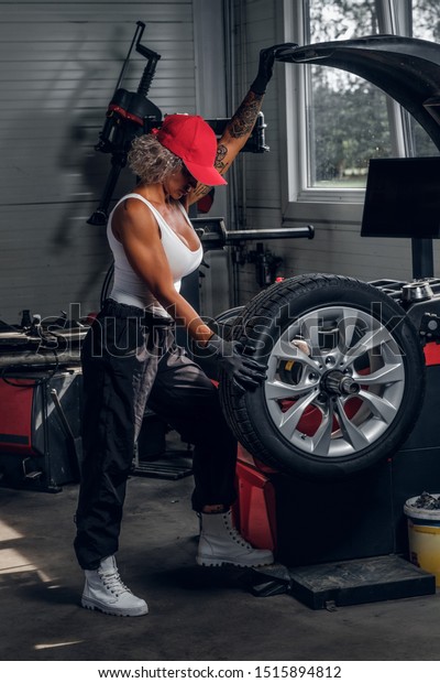 Professional female auto mechanic is fixing\
broken car at auto workshop near\
window.