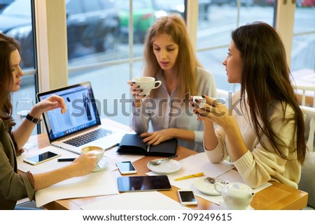 Professional female business partners concentrated on discussing details of collaboration during coffee break in cafe, young women choosing strategy for new clothing colection marketing on website