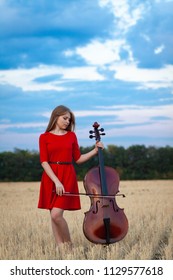 Professional Female Cello Player In Red Dress With Instrument Outdoors