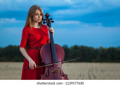 Professional Female Cello Player In Red Dress With Instrument Outdoors