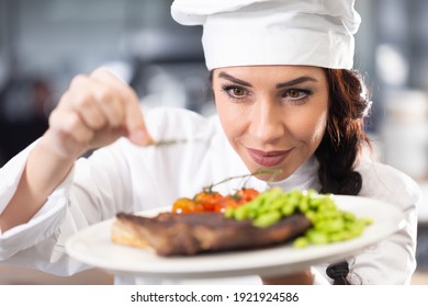 Professional female chef in a hat makes final touches on a freshly made steak before serving.