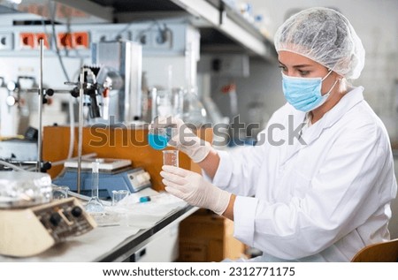 Professional female chemist investigating behavior of blue liquid reagents while working in modern laboratory