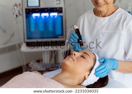 Professional female cosmetologist doing hydra-facial procedure in cosmetology clinic. Doctor using hydra vacuum cleaner. Rejuvenation and cosmetology concept  Stock fotó © 