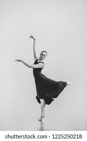 Professional Female Dancer In Black Dress Jumping Dancing In Studio Isolated Background. Beautiful Young Woman Girl Posing Indoors Natural Light Black And White Copy Space Choreography Card Arts