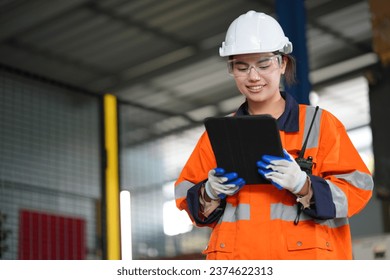 Professional female engineer in hard hat and safety glasses examining modern machine equipment at plant and taking notes on tablet computer - Powered by Shutterstock