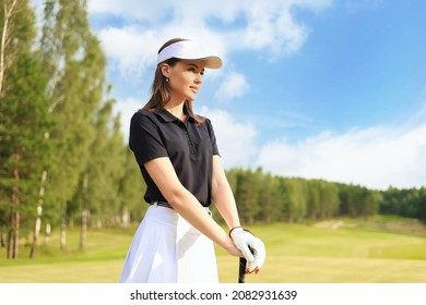 Professionelle Golferin, die einen Golfclub auf dem Feld hält und einen Blick weg hat. Junge Frau, die an einem sonnigen Tag auf dem Golfplatz steht.