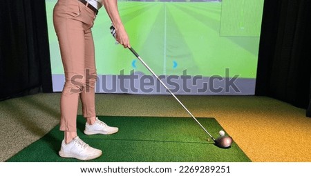 Professional female golfer playing golf indoors on golf simulator closeup. Driving range with screen and golf course