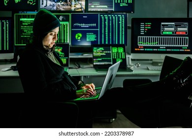 Professional Female Hacker Typing Virus Code On Laptop For Cyber Attack In Dark Room With Multiple Monitors On The Background