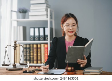 Professional female lawyer at her desk with legal books and scales, reading and taking notes in an office setting. - Powered by Shutterstock