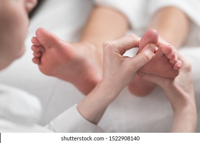 Professional Female Masseur Giving Reflexology Massage To Woman Foot.