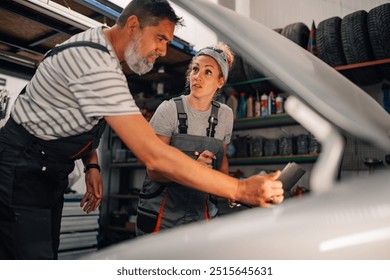 Professional female mechanic discussing with her colleague repairman at auto mechanic workshop while doing car engine diagnostics on little laptop. Colleagues technicians servicing car at workshop. - Powered by Shutterstock