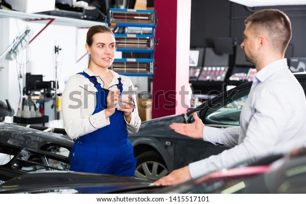 Professional\
female mechanic discussing with male client and recording list of\
works on car repair in auto repair shop\
\
