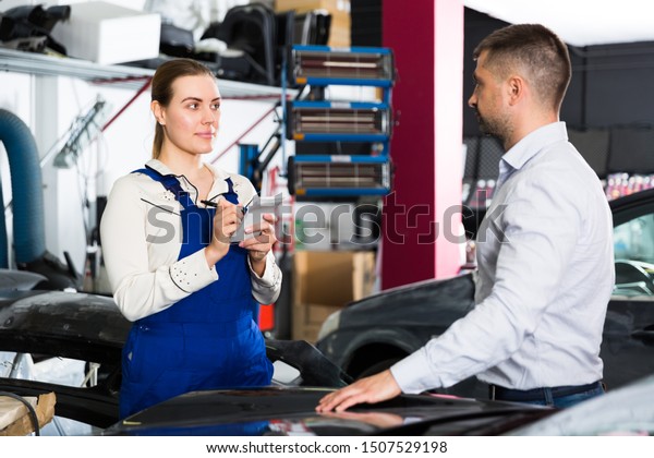 Professional\
female mechanic discussing with male client and recording list of\
works on car repair in auto repair shop\
\
