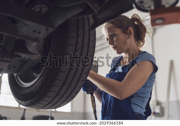 Professional female mechanic doing a wheel\
replacement in the auto repair\
shop