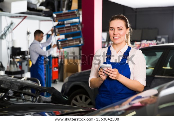 Professional female mechanic recording list\
of works on car repair in auto repair shop\
