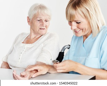 a professional female nurse or caregiver measure the pulse of an old women or grandmother in a wheechair at a table with a clock in the hand