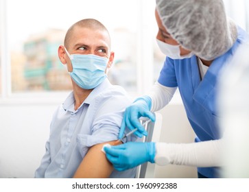 Professional Female Nurse Injecting Vaccine In Shoulder Of Male Patient During Covid Vaccination In Clinic Or Hospital