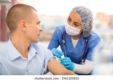 Professional Female Nurse Injecting Vaccine In Shoulder Of Male Patient During Covid Vaccination In Clinic Or Hospital