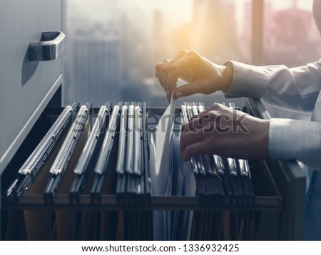 Professional female office clerk searching files and paperwork in the filing cabinet