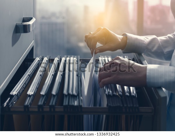 Professional female office clerk searching files\
and paperwork in the filing\
cabinet