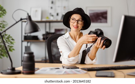 Professional female photographer reviewing photos on camera at office. Caucasian woman wearing trendy hat, white shirt and eyeglasses. - Powered by Shutterstock