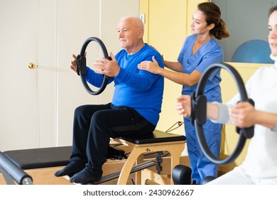 Professional female physiatrist controlling older man exercising with pilates ring to strengthen muscles. Physical medicine and rehabilitation concept - Powered by Shutterstock