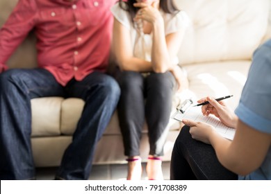 Professional female psychologist making notes of married couple during therapy session
