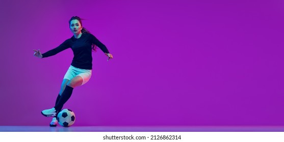 Professional female soccer player dribbling football ball isolated on purple studio background in neon light. Concept of sport, action, motion, fitness. Young sportive girl training. Flyer