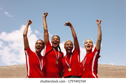 Professional female soccer players celebrating a victory on a sports arena. Group of woman football players screaming and punch air after winning the championship on sports field. - Powered by Shutterstock