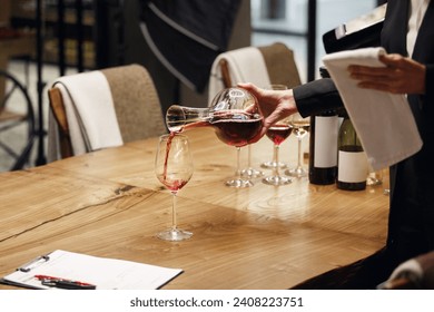 Professional female sommelier pours red wine from decanter to the glass, close up image. Woman waiter pouring alcoholic drink being in cellar of wine shop. - Powered by Shutterstock