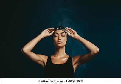 Professional female swimmer with eyes closed on dark background. Woman in black swimming costume with holding swimming goggles. - Powered by Shutterstock