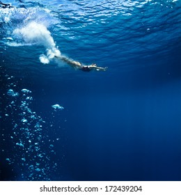 professional female swimmer shooted just after jump into deep blue ocean with air bubbles trail