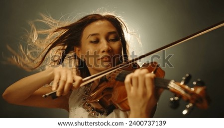 Professional female violin player performing an amazing solo during concert, spotted by light on smoked black background 