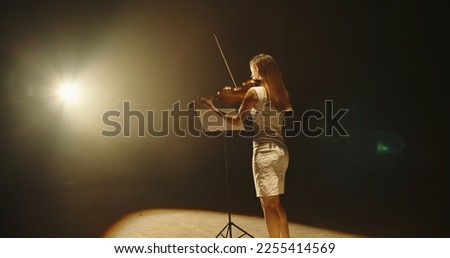 Professional female violinist performing a solo concert on stage. Professional violin player spotted by light on black background 