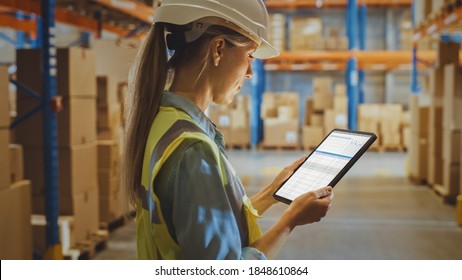 Professional Female Worker Wearing Hard Hat Uses Digital Tablet Computer with Inventory Checking Software in the Retail Warehouse full of Shelves with Goods. Delivery, Distribution Center. - Powered by Shutterstock