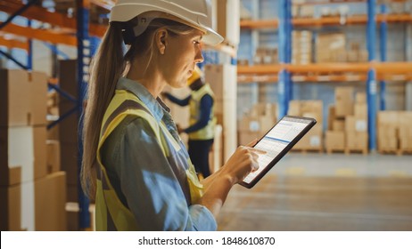 Professional Female Worker Wearing Hard Hat Uses Digital Tablet Computer with Inventory Checking Software in the Retail Warehouse full of Shelves with Goods. Delivery, Distribution Center. - Powered by Shutterstock