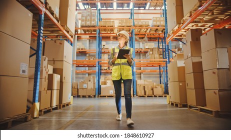 Professional Female Worker Wearing Hard Hat Checks Stock and Inventory with Digital Tablet Computer Walks in the Retail Warehouse full of Shelves with Goods. Working in Delivery, Distribution Center