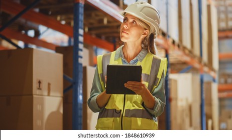 Professional Female Worker Wearing Hard Hat Checks Stock And Inventory With Digital Tablet Computer In The Retail Warehouse Full Of Shelves With Goods. People Working In Logistics Distribution Center