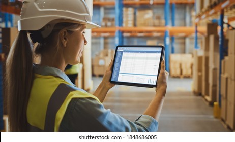 Professional Female Worker Wearing Hard Hat Uses Digital Tablet Computer with Screen Showing Inventory Checking Software in the Retail Warehouse full of Shelves with Goods. Over the Shoulder View - Powered by Shutterstock