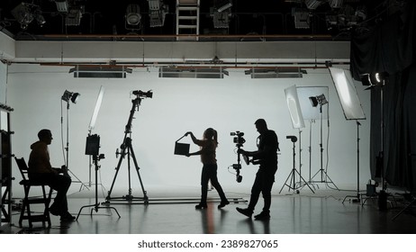 Professional filming pavilion with a white cyclorama. Shooting of a girl in a red dress who sings into a retro microphone. Director, Cameraman and crew in Backstage. - Powered by Shutterstock