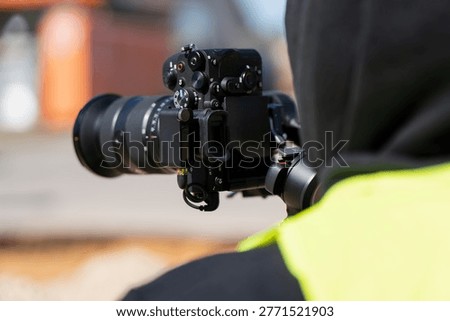 Professional filmmaker using mirrorless camera with wireless transmitter on handheld gimbal to record construction site progress for industrial documentary and media production