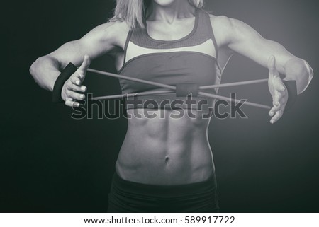 One young middle age athletic woman at crossfit training, exercising with trx suspension fitness straps over dark background, front view, looking up