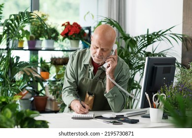 Professional Florist Working In His Plant Shop, He Is Talking On The Phone And Taking Orders, Small Business Concept