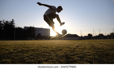 Professional footballer juggling soccer ball on stadium at sunset. Young man kicking ball at green field. Sportsman practicing tricks at meadow with sunlight at background. Freestyle football concept - Powered by Shutterstock