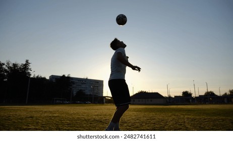 Professional footballer juggling soccer ball on stadium at sunset. Young man kicking ball at green field. Sportsman practicing tricks at meadow with sunlight at background. Freestyle football concept - Powered by Shutterstock