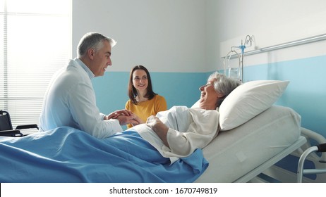 Professioneller, freundlicher Arzt, der eine ältere Patientin auf einem Krankenhausbett trifft, und ihre Tochter, Vorsorgekonzept