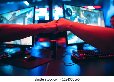 Professional gamer greeting and support team fists hands online game in neon color blur background. Soft focus, back view.