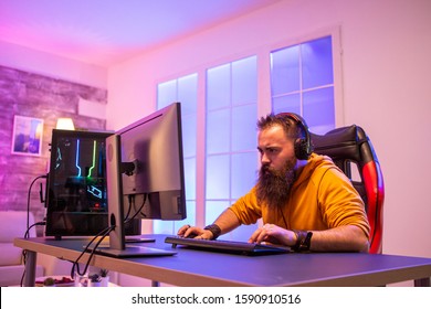 Professional Gamer With Long Beard In Front Of Powerful Gaming Rig In Room Full Of Neon Lights