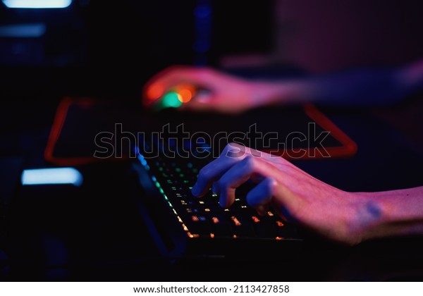 Professional gamer play computer video game in\
dark room, use neon colored rgb mechanical keyboard, place for\
cybersport gaming
