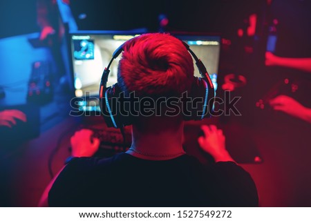 Professional gamer playing online games tournaments pc computer with headphones, Blurred red and blue background.
